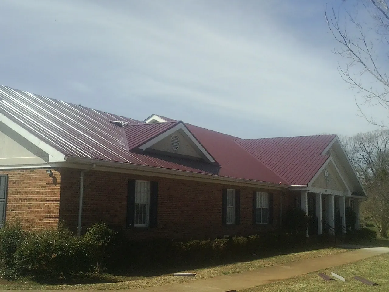 Red metal roof with gabled entries on a long brick building, from a Hail Damage Roof Repair job in Bunker Hill
